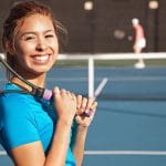 a woman enjoying tennis lessons in her area. Racquet of her shoulder smiling at the camera